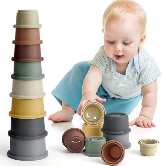 One year old baby sitting on the floor playing with colorful stacking cups and building a tall tower
