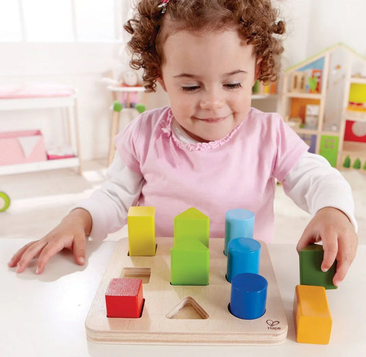 Preschool child placing colorful geometric shapes into a wooden shape sorting puzzle board